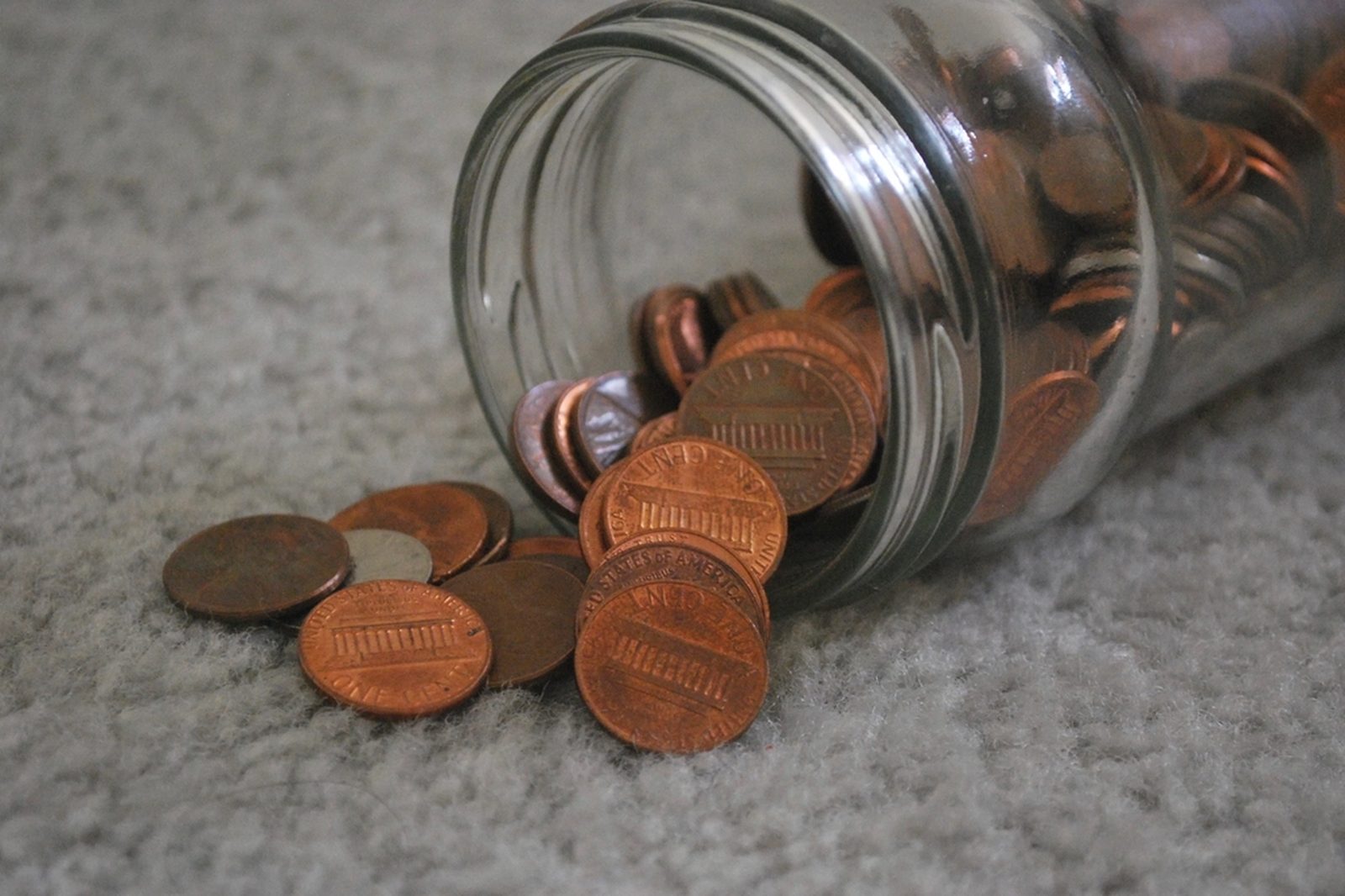 A glass jar tipped on its side with copper pennies spilling onto a carpet